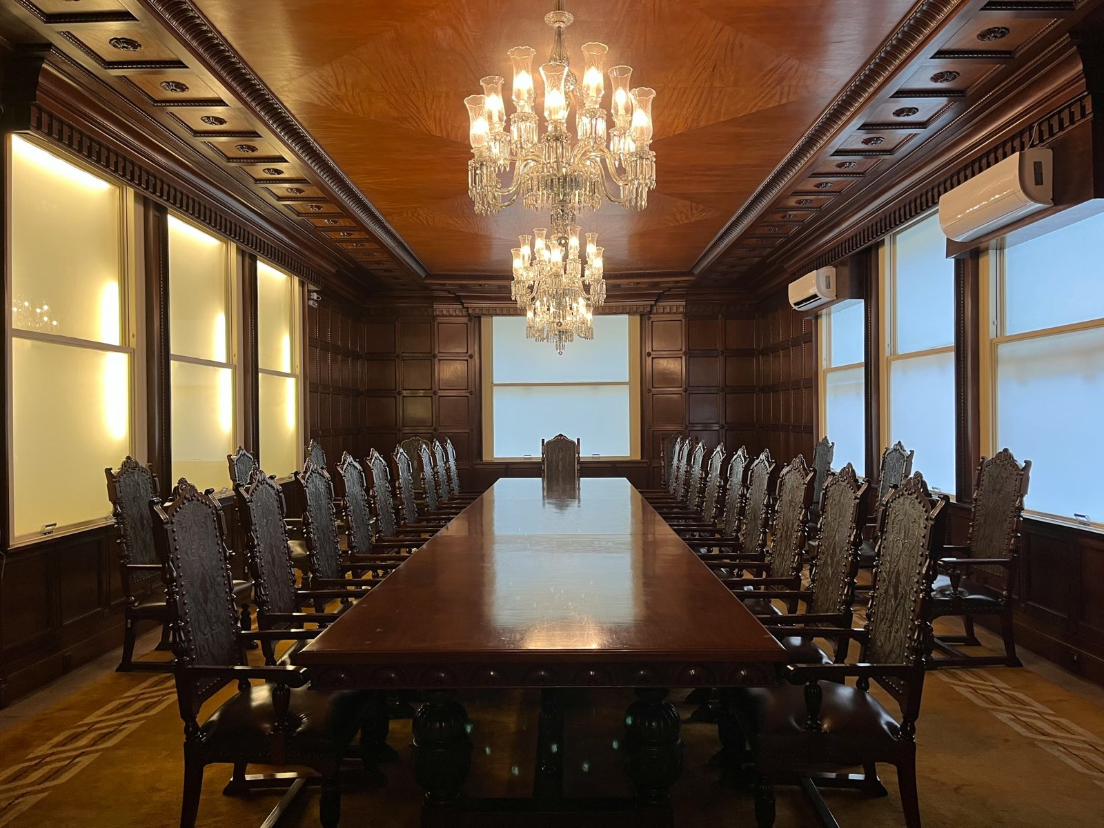 A wood-panelled boardroom under chandeliers