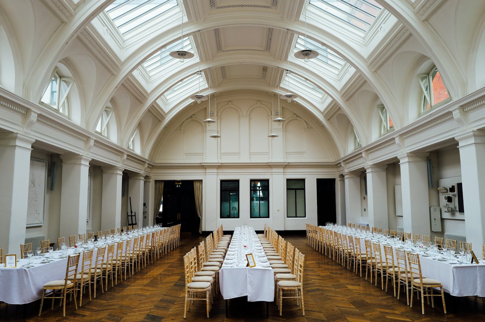 A vaulted hall set with long tables under skylights
